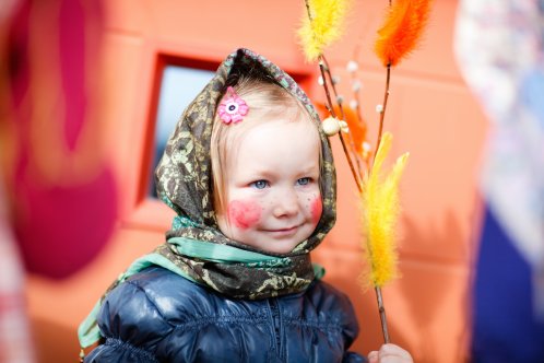 Barn utklädd till påskgumma med fjädrar, huckle och röda kinder. 