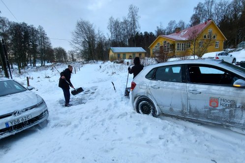 En person står bredvid en bil och skottar snö med en snöskyffel. På bilden syns mycket snö.