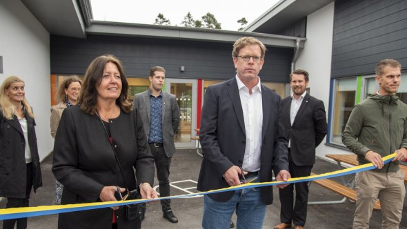 Två personer som klipper ett band för att inviga förskolan. Bakom dem syns flera andra personer.