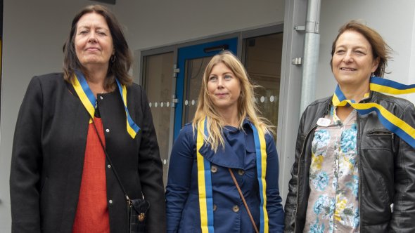 En bild på tre kvinnor med färgglada band runt halsen.