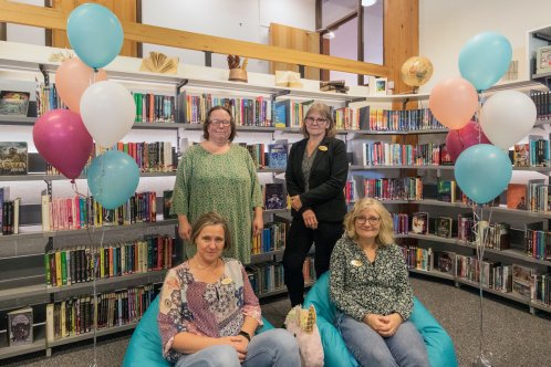 Fyra kvinnor på biblioteket. I bakgrunden syns ballonger och böcker i bokhyllor.