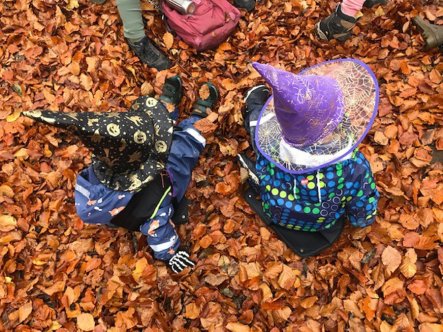Barn i häxhatt sitter på torra löv i skogen..