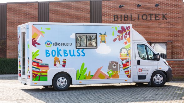 Bild på bokbussen, en vit minibuss med färgglada illustrationer på