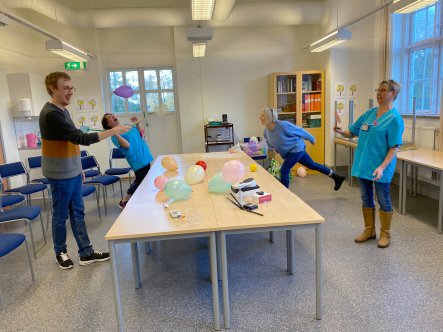 Fyra personer spelar "ballong-pingis" med flugsmällare över två bord.