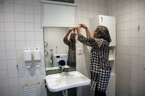 En kvinna drar ner en rullgardin för att dölja en spegel över ett handfat.