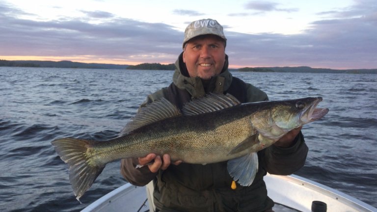 Mitt ute på sjön sitter sportfiskaren Michael Magnusson i en båt. Han håller upp en stor, nyfångad gös och ser nöjd och glad ut. Gös kan du fiska i Vaxsjön, Tjörnarpssjön och Ringsjön.