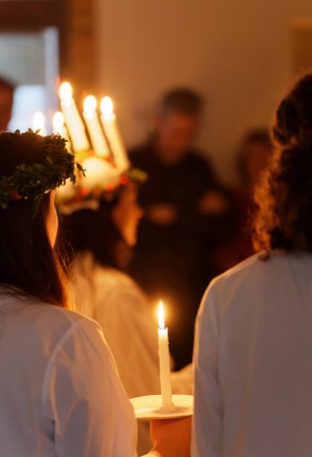 Lucia med levande ljus i håret. Två tärnor i förgrunden.