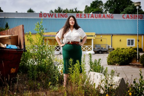 Kvinna står bland ogräs och väster framför en gul byggnad med orden "bowling restaurang" på.