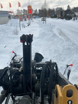 En maskin röjer bort snön på en väg med snödrivor.